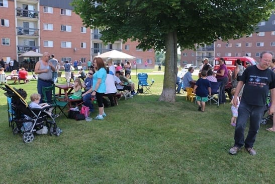 Large lawn with residents gathered in lawn chairs eating barbecue