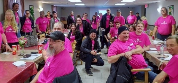 Room full of people wearing pink shirts and eating lunch