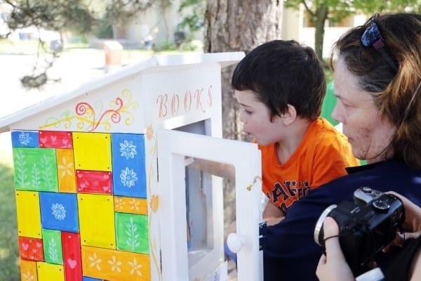 Child and mother look into a wooden box that is a new book lending library